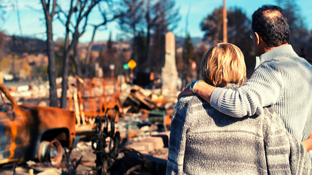 Bushfire recovery assistance (couple embracing looking at what is left of their property after bushfires)